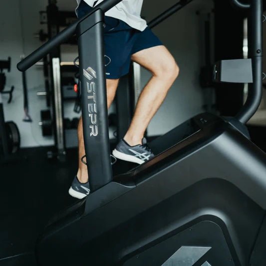 Close-up of a male athlete's legs and shoes on the STEPR+ Stair Climber, highlighting the floating step design and sturdy foot platform.