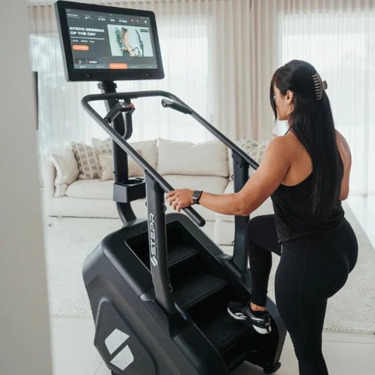Female athlete stepping onto the STEPR+ Stair Climber in a room in her house, demonstrating easy access and compact design for home use.