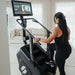 Female athlete stepping onto the STEPR+ Stair Climber in a room in her house, demonstrating easy access and compact design for home use.