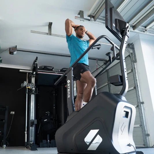 Male athlete working out on the STEPR+ Stair Climber, viewed from the floor looking up, emphasizing the compact design and 27” HD touchscreen.