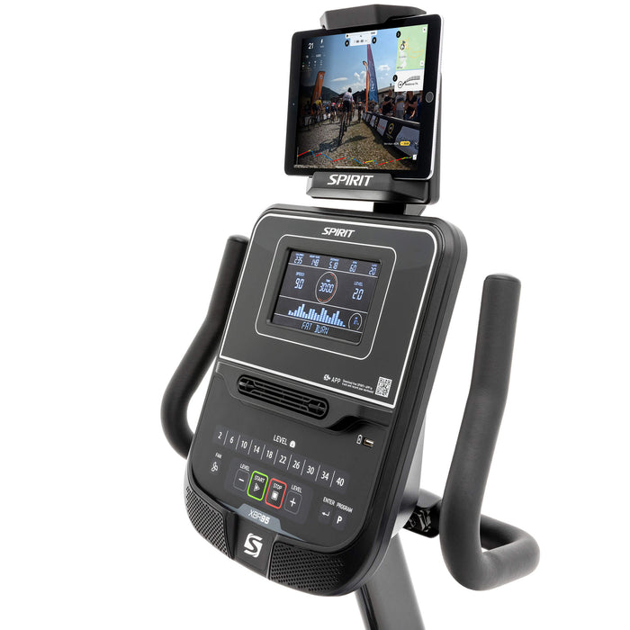 Close-up view of the Spirit Fitness XBR95 Recumbent Bike's console displaying workout data, with a tablet on the holder running a racing app during a workout session.