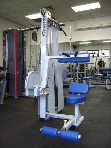 Legend Fitness Ab Crunch Machine 941 with white frame and blue upholstery in a gym setting, featuring adjustable seat, ankle rollers, and full-range crunch motion.