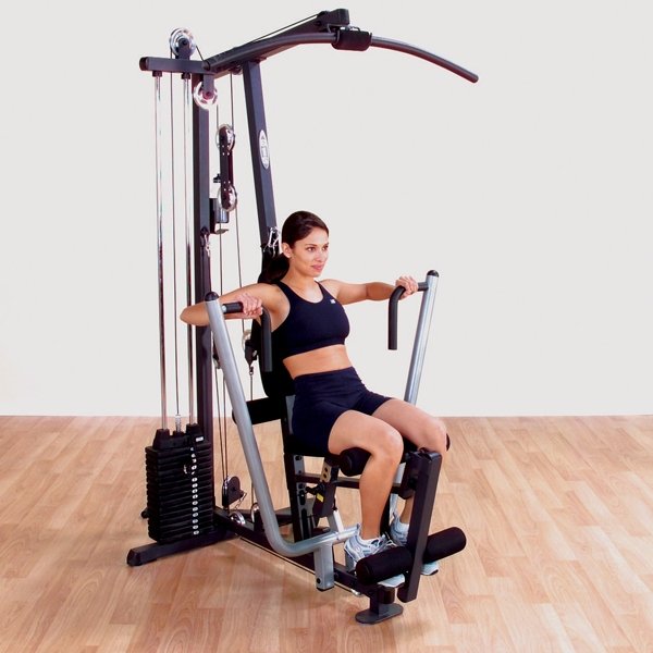 Female athlete performing a wide grip seated chest press on a Body-Solid G1S Multi-Station Home Gym, focusing on chest and tricep muscle development.