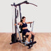 Female athlete performing a wide grip seated chest press on a Body-Solid G1S Multi-Station Home Gym, focusing on chest and tricep muscle development.